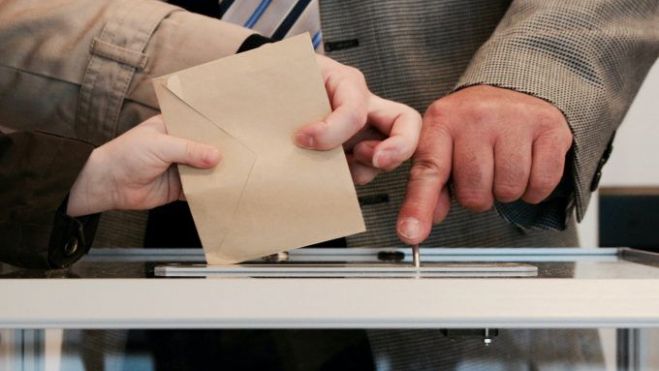 Una persona introduce el sobre con sus papeletas en una urna un día de elecciones Una persona introduce el sobre con sus papeletas en una urna un día de elecciones