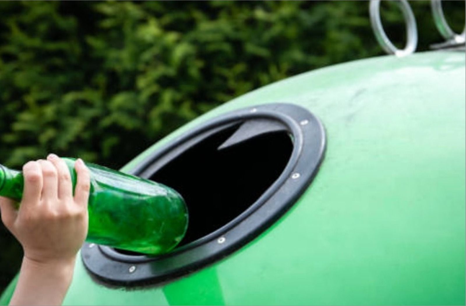 Una persona recicla una botella de vidre en el contenidor verd