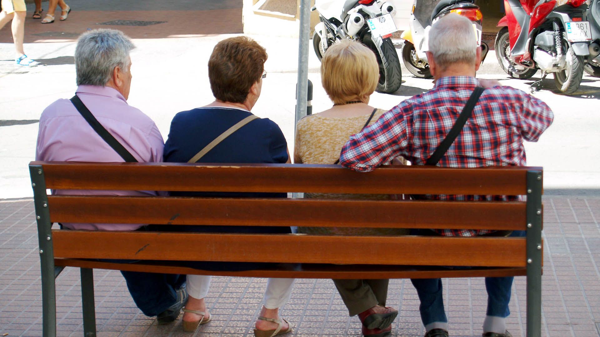 Dos parejas de personas mayores sentadas en un banco en la calle