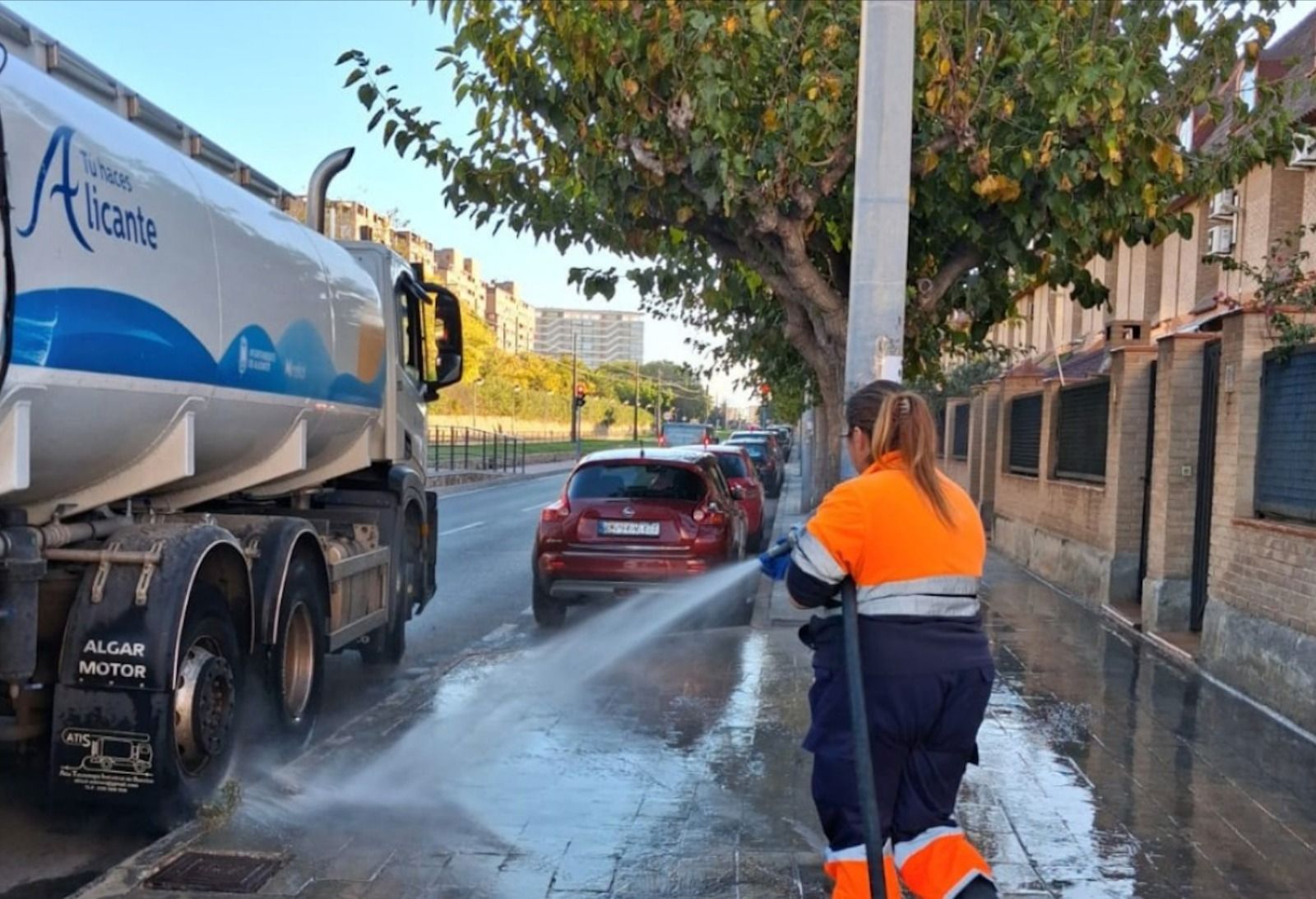 Una operària de la neteja a Alacant realitza un aigualeig en un carrer de la platja de Sant Joan