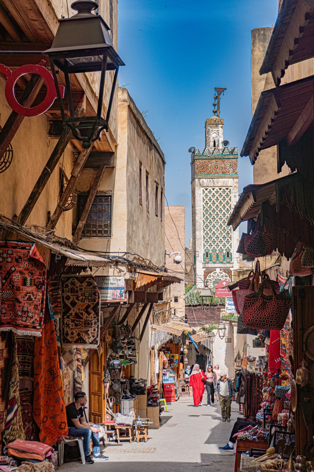 Calle estrecha y bulliciosa de Fez, con tiendas, textiles y un minarete a la vista
