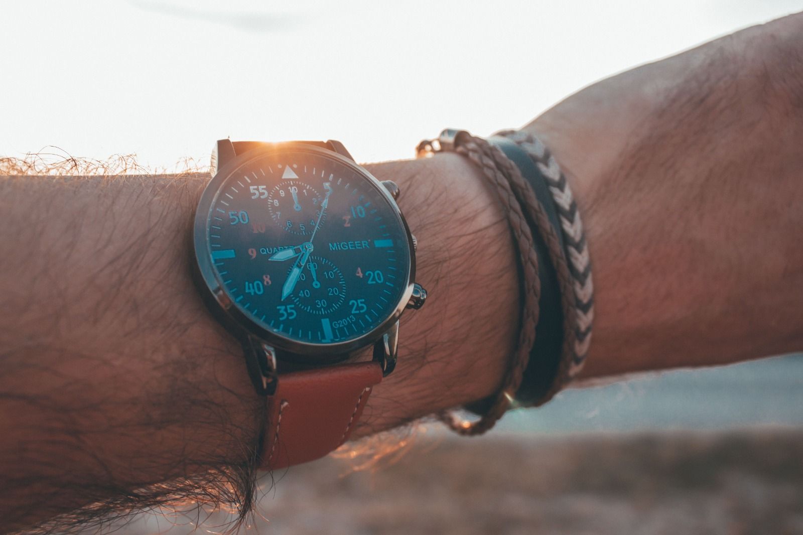 Primer plano de un reloj y pulseras en la muñeca con un fondo de atardecer Primer plano de un reloj y pulseras en la muñeca con un fondo de atardecer